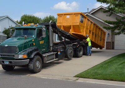 Veit Disposal picking up a roll-off dumpster rental from a residential driveway.